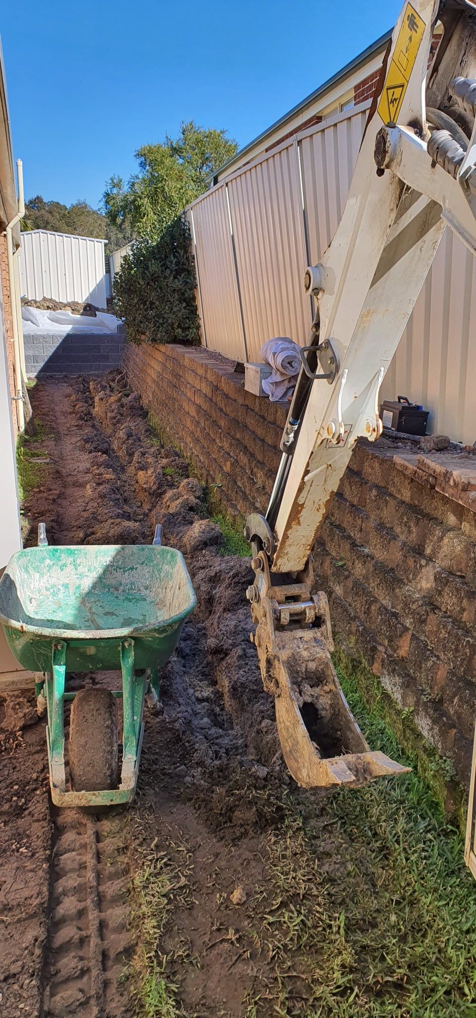 A wheelbarrow is sitting next to an excavator in a yard.