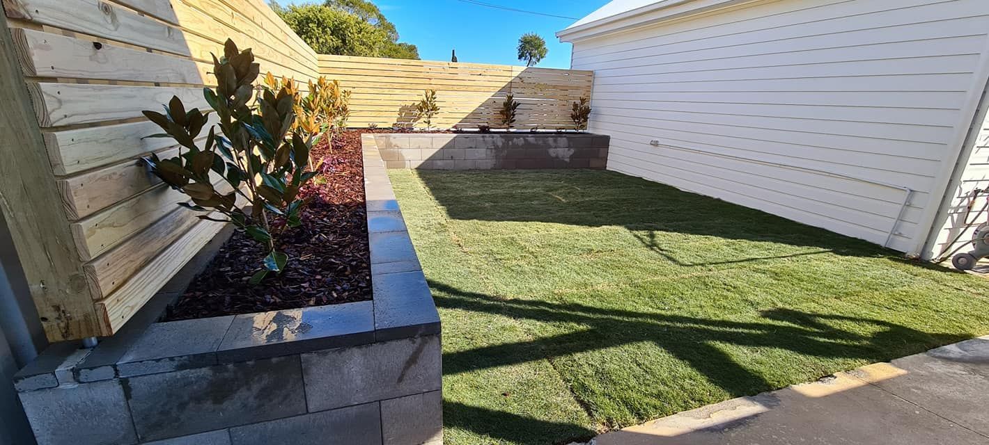 A backyard with a planter and a lawn in front of a house.