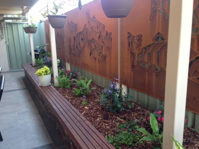 A wooden bench with flowers and potted plants in front of a fence.
