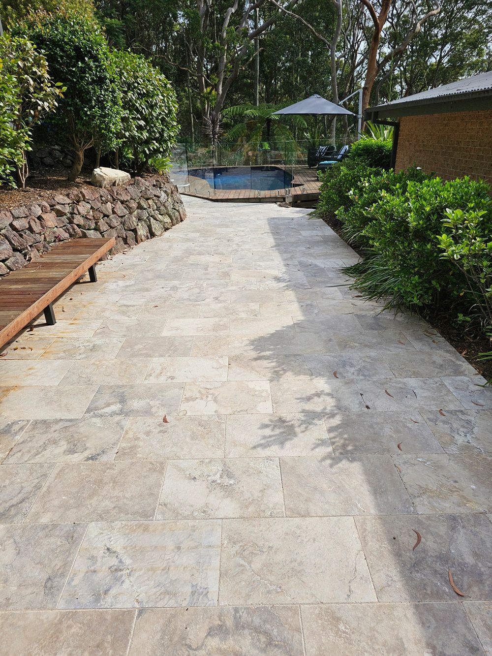A stone walkway leading to a pool in a backyard.