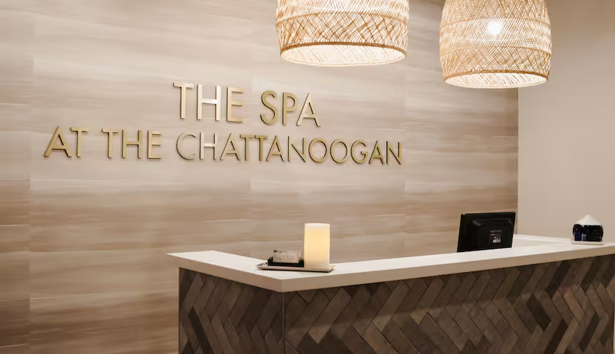 Reception desk at The Spa at The Chattanoogan, gold lettering on a beige wall, with woven pendant lights.