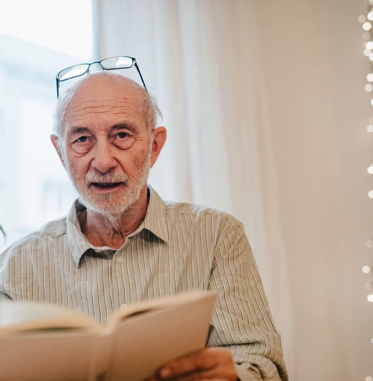 Older man with glasses on head, reading a book, looking directly at the viewer.