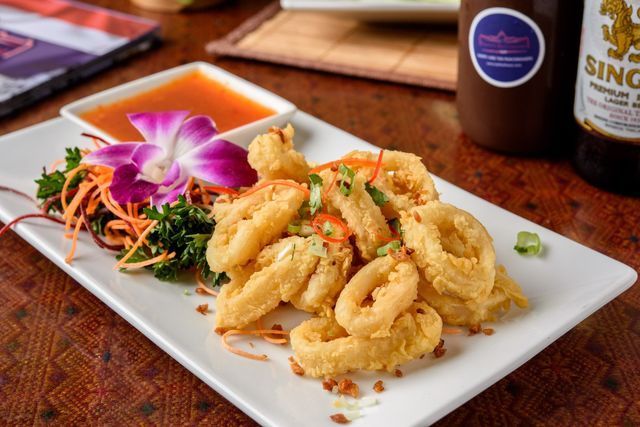 A white plate topped with fried calamari and vegetables next to a bottle of beer.