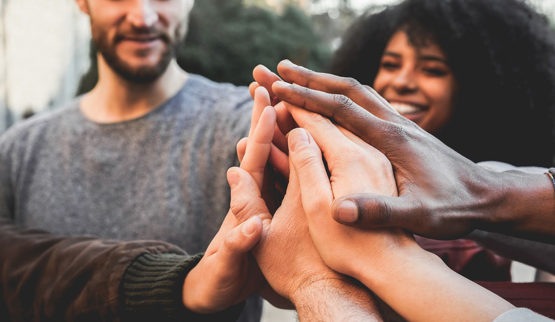 Hands of several people in a high-five, with smiles and out-of-focus background.