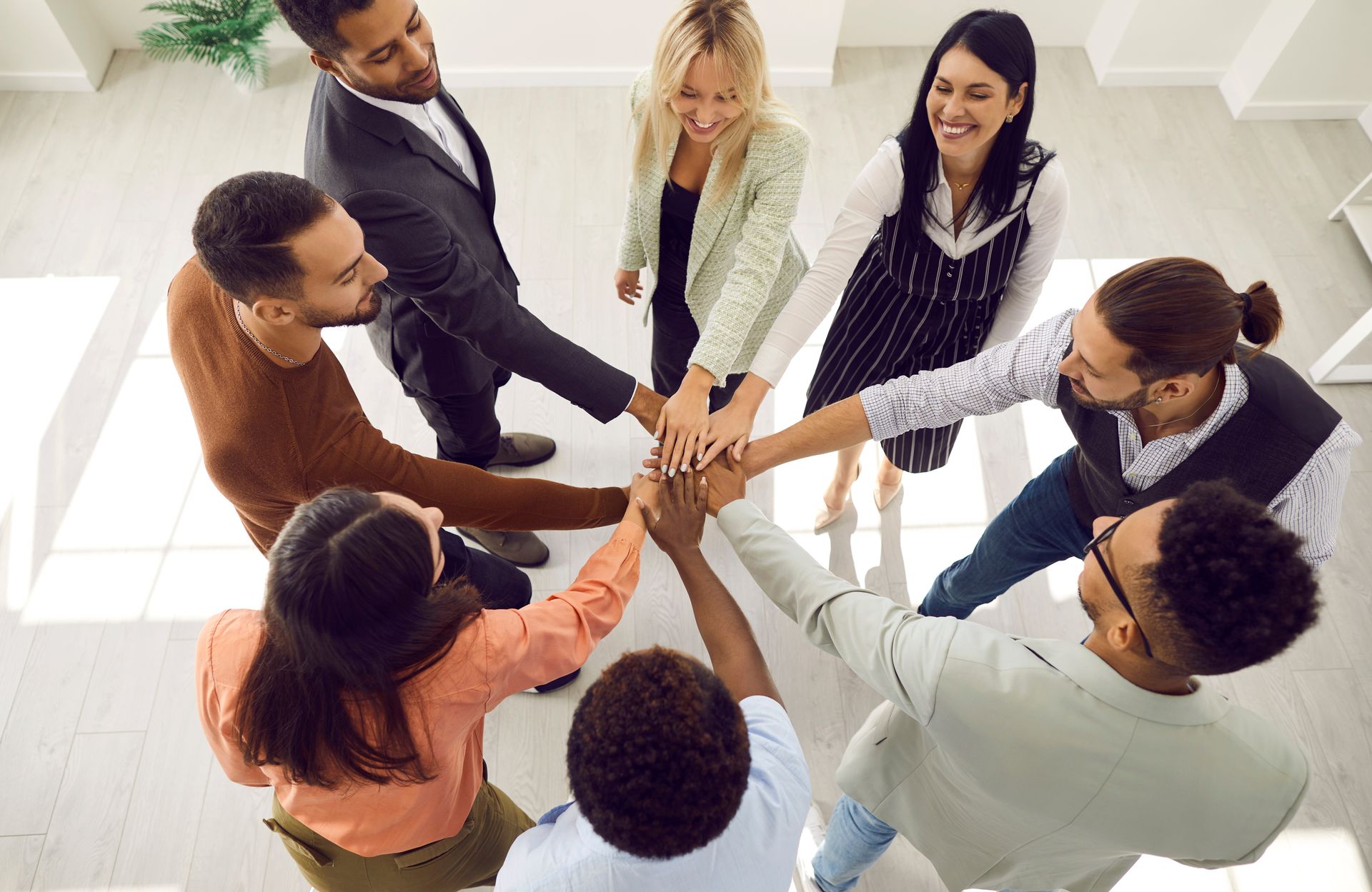 Group of people with hands together in a circle, smiling, indoors.