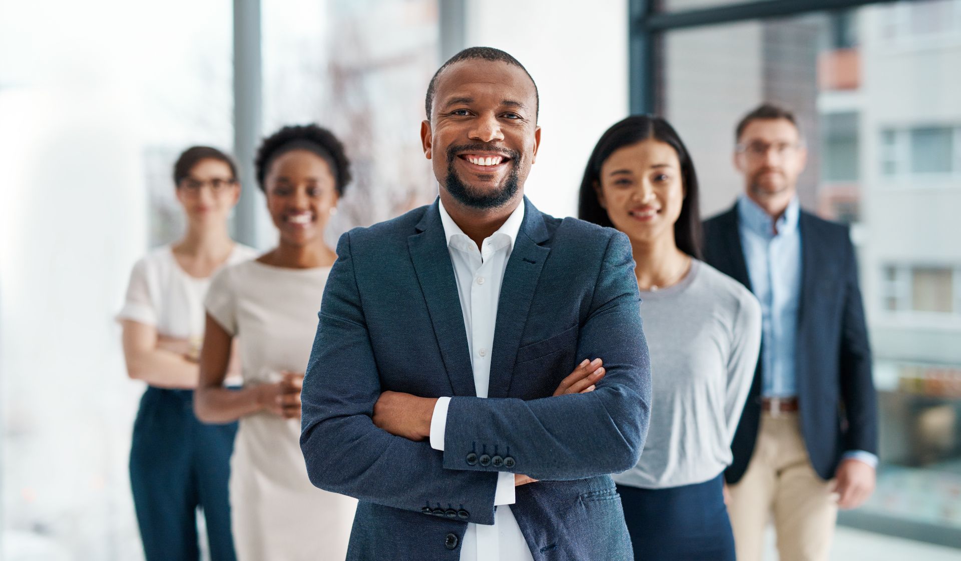 Group of people in business attire, smiling in an office setting, with crossed arms.
