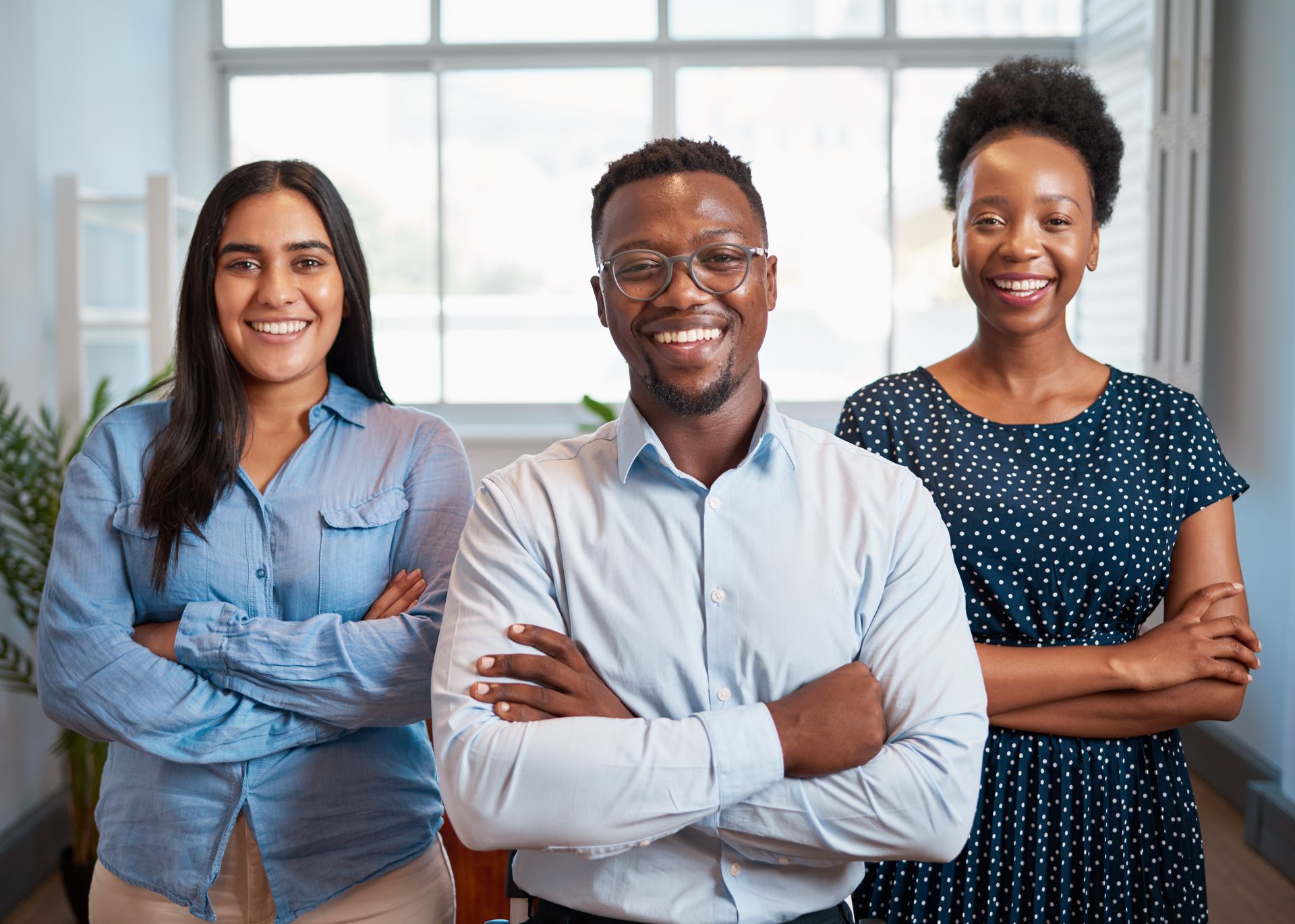 Three smiling people with crossed arms in an office setting.
