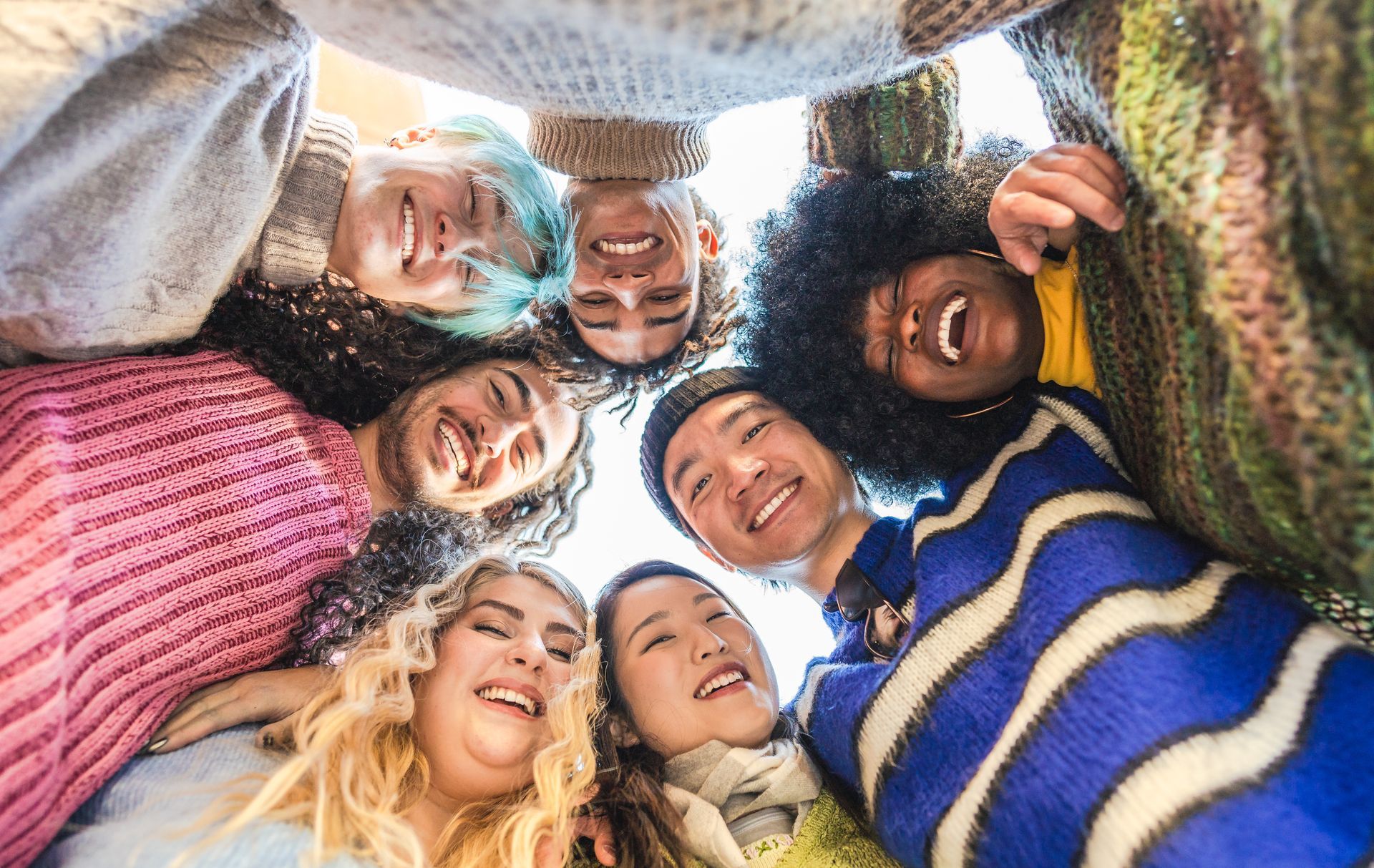 Group of smiling people looking down from a circle, various skin tones and hair, outdoors.