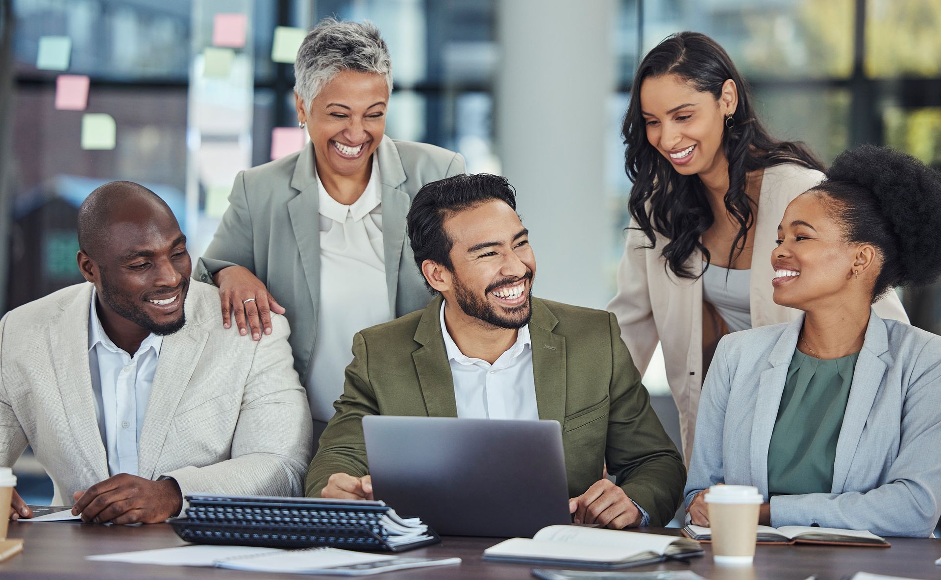 Business team gathered around a laptop, smiling. Office setting, focused collaboration.
