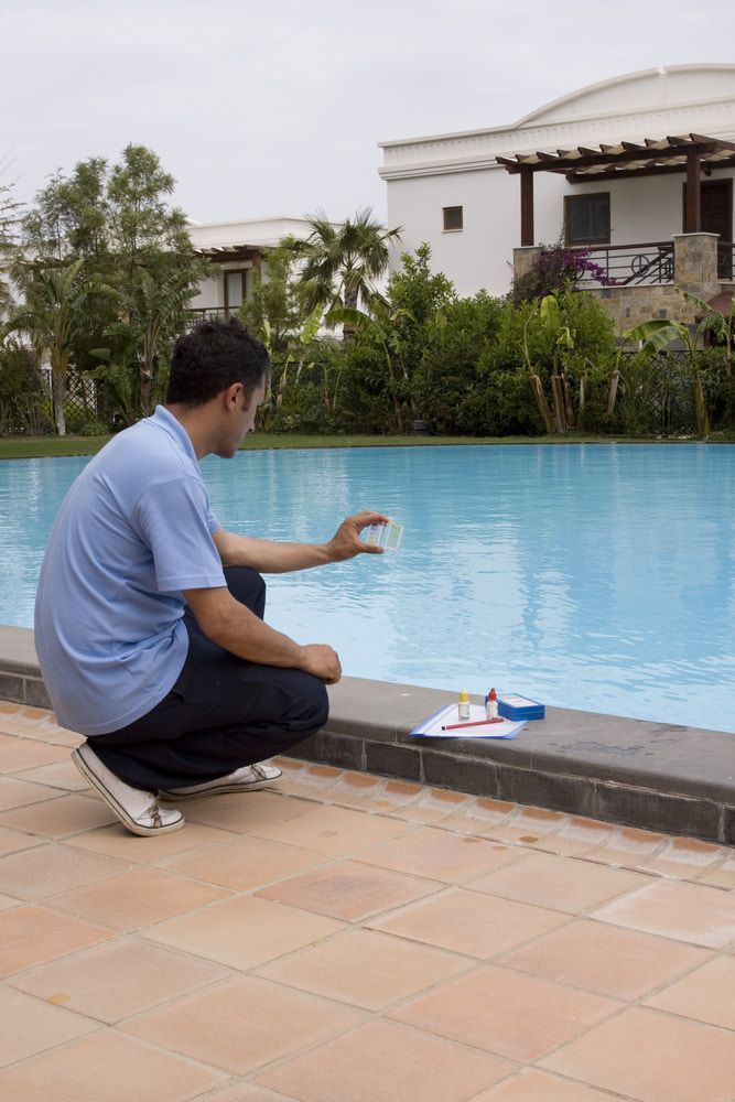 A Man Is Kneeling On The Edge Of A Swimming Pool — Aquatic Pool & Spa Services In Yeppoon, QLD