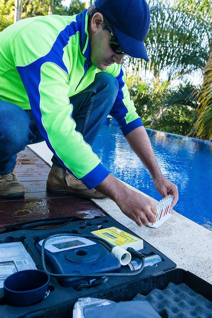 A Man Is Kneeling On The Edge Of A Swimming Pool — Aquatic Pool & Spa Services In Yeppoon, QLD