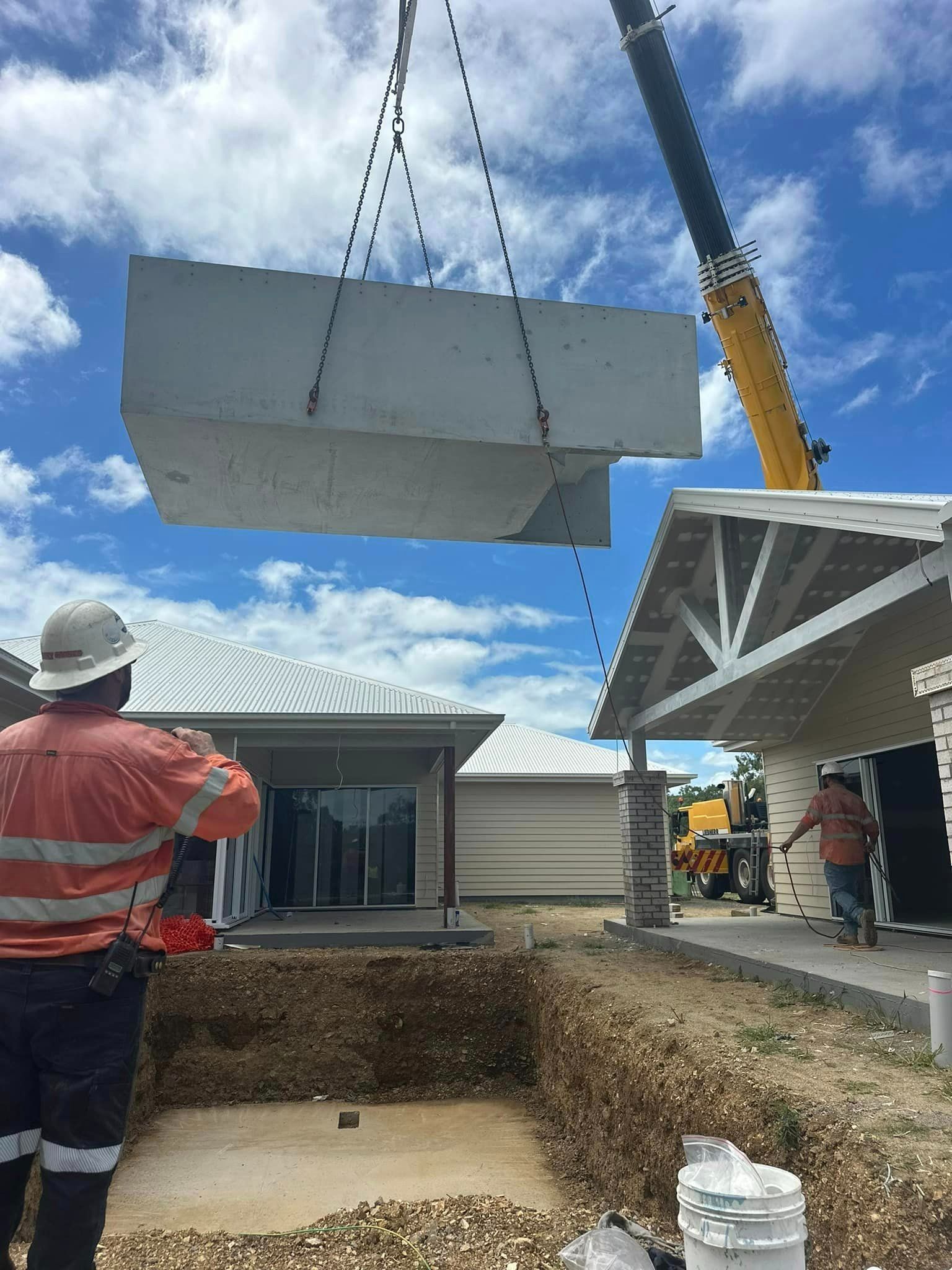 A Crane Is Lifting A Large Piece Of Concrete Into A Hole In Front Of A House — Aquatic Pool & Spa Services In Gladstone, QLD