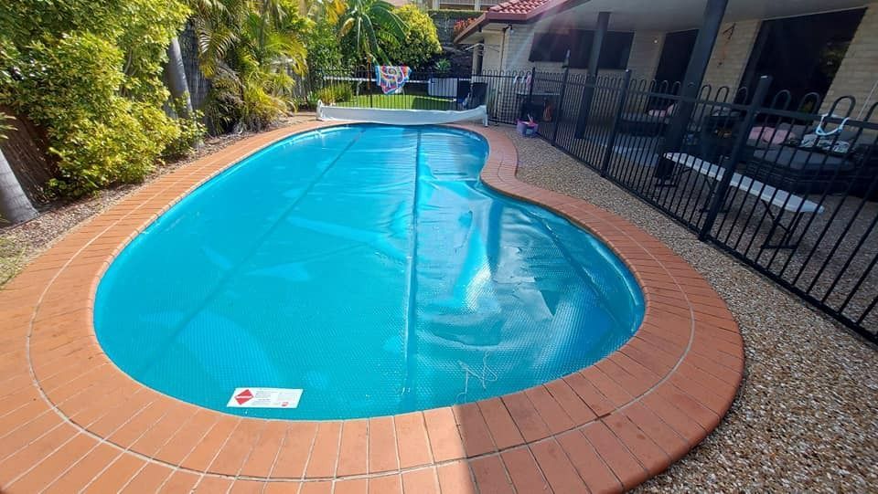 A Large Swimming Pool Is Surrounded By A Fence And A House — Aquatic Pool & Spa Services In Yeppoon, QLD