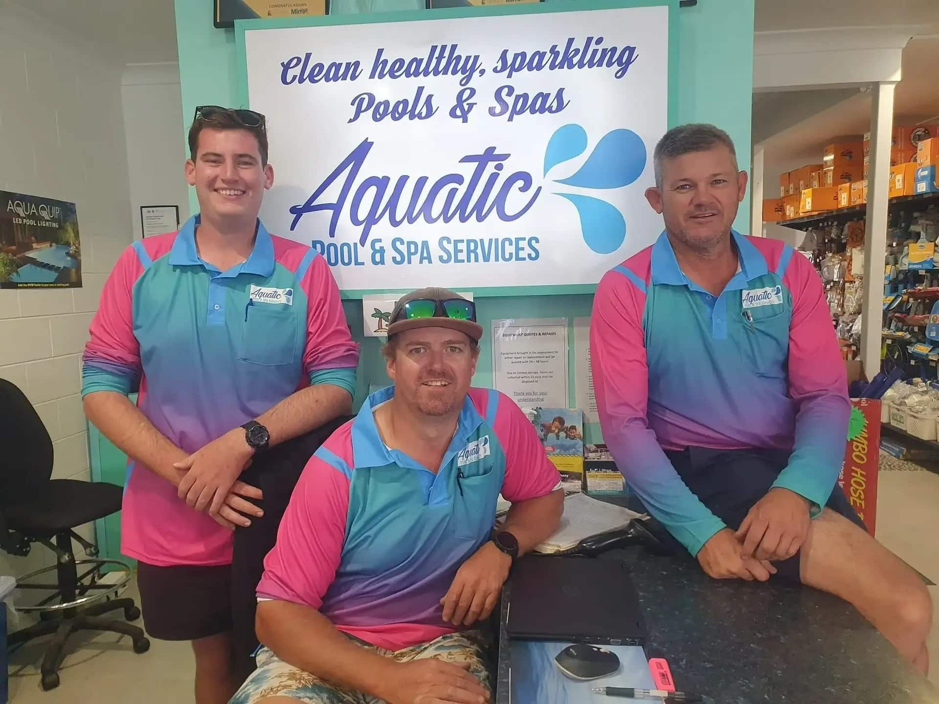 Three Men Are Posing For A Picture In Front Of A Sign — Aquatic Pool & Spa Services In Yeppoon, QLD