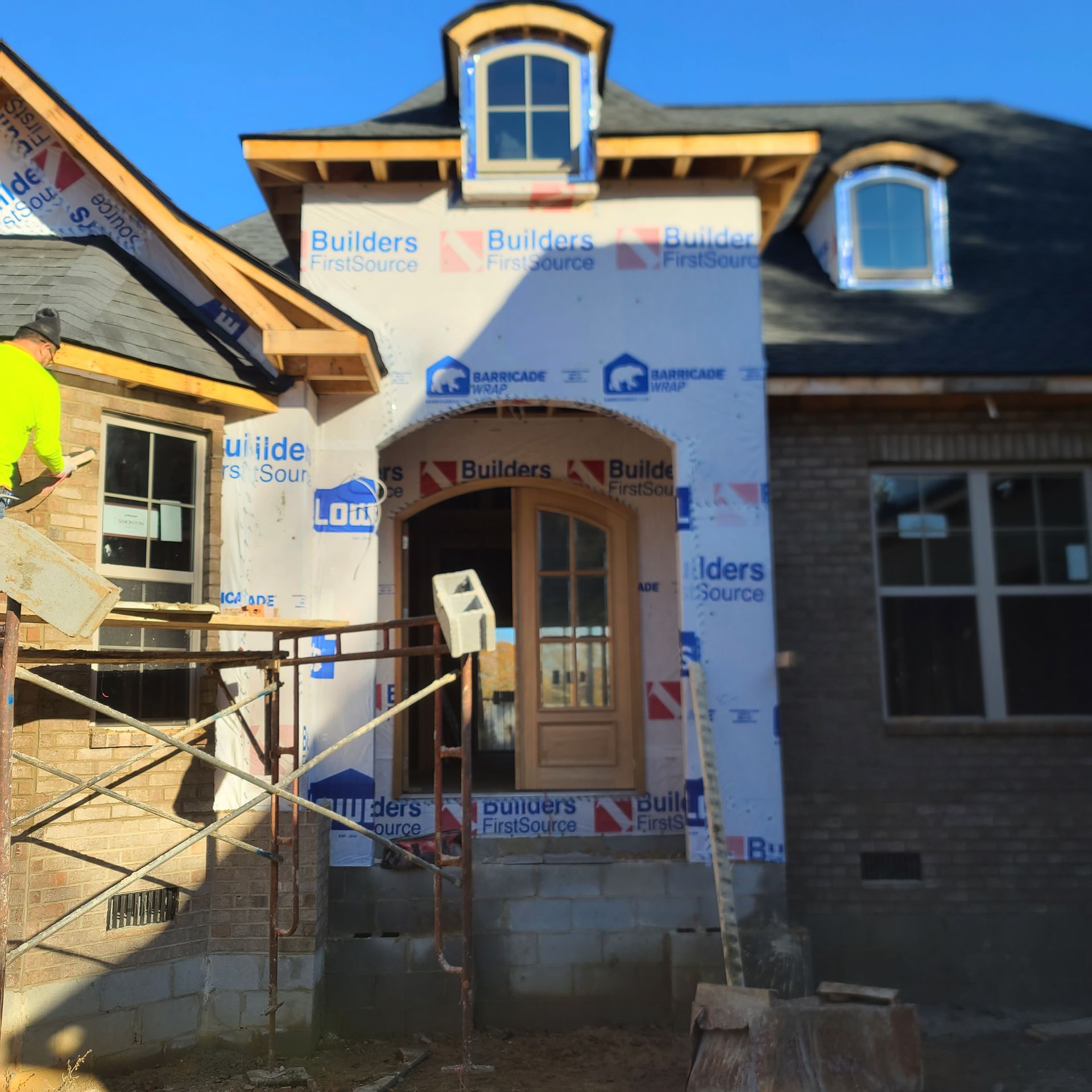 Construction of a brick house with a wooden door and two arched windows. Blue weather protection is visible.