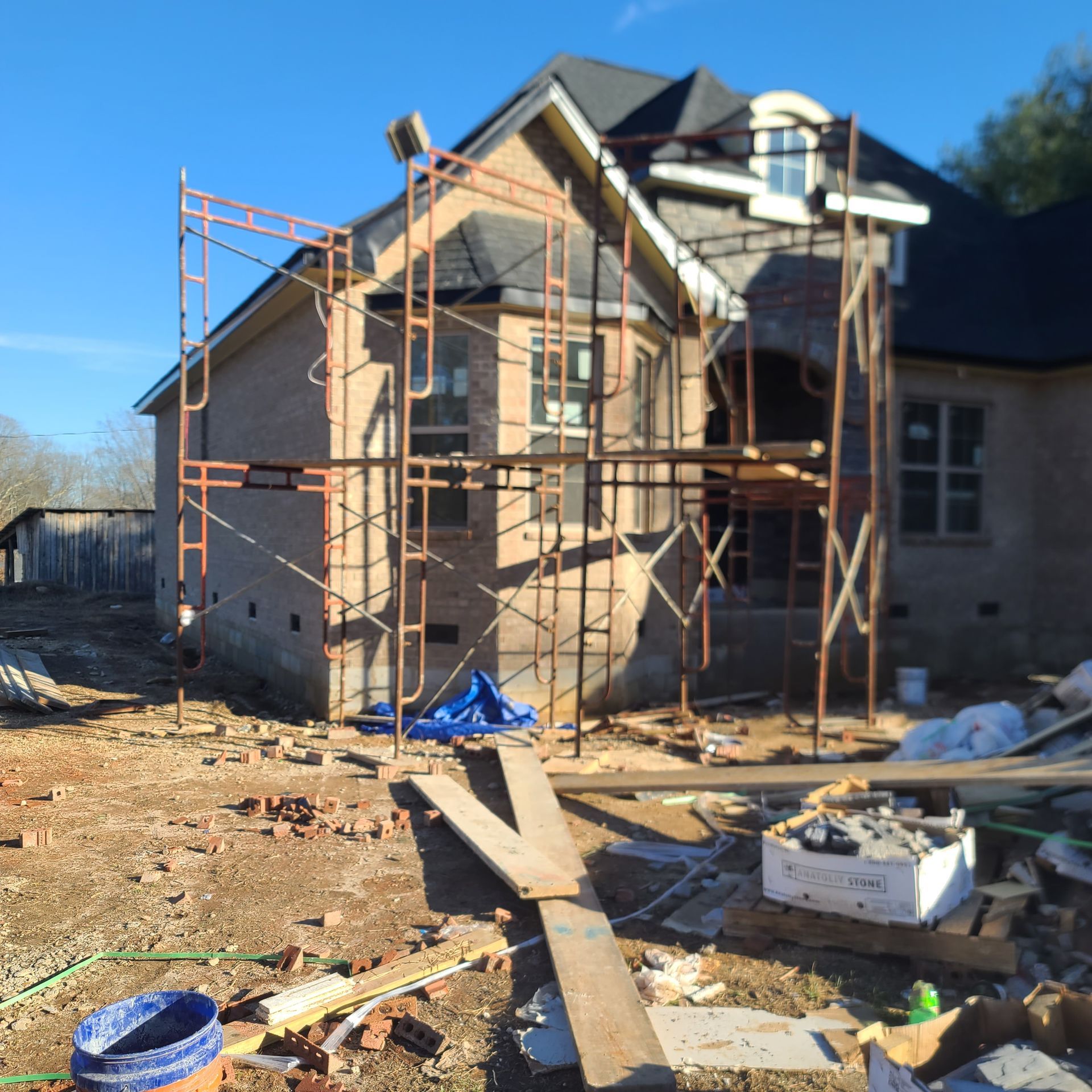 Construction of a two-story brick house with scaffolding, under a blue sky.