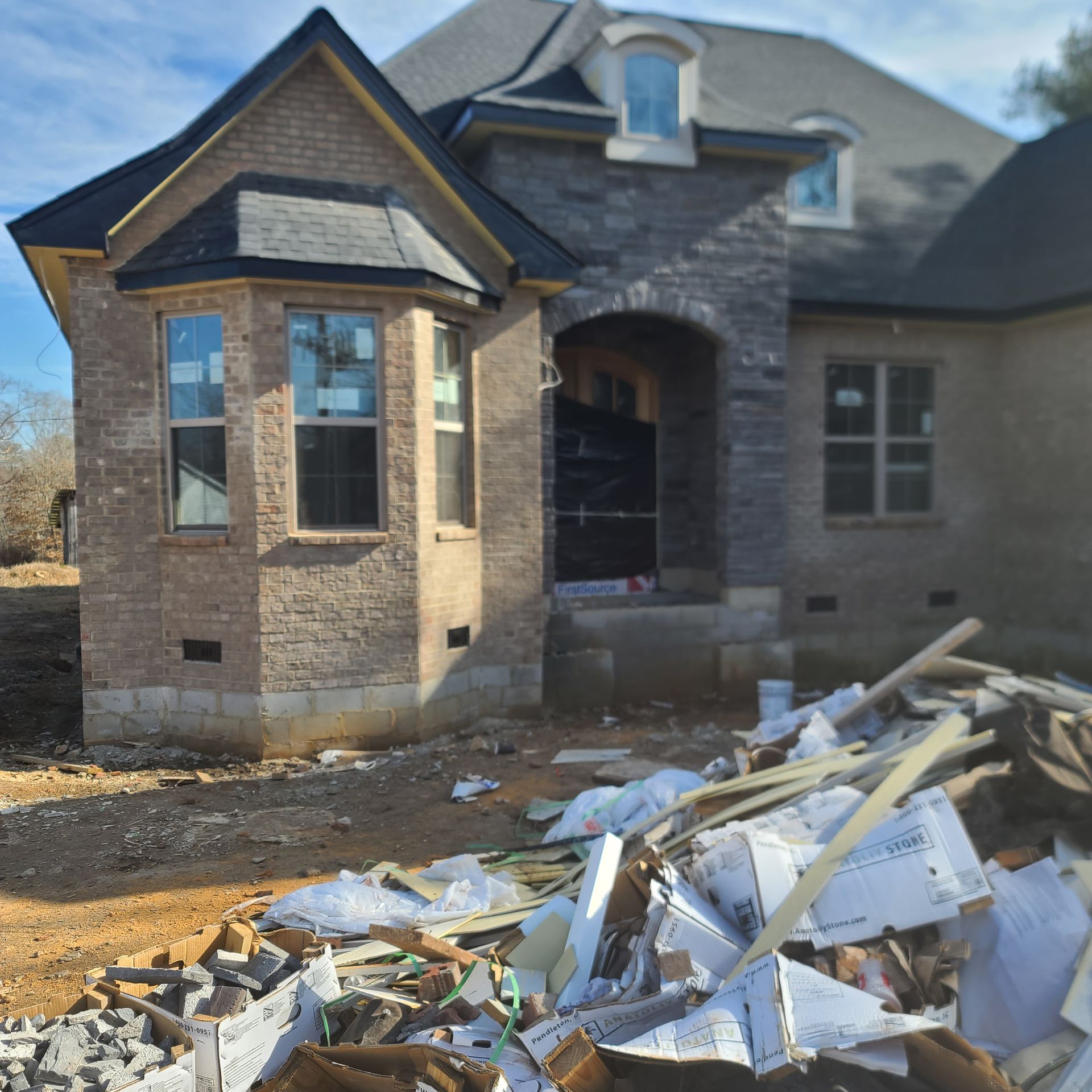 Construction site: partially built brick home with stone accents, bay window, and debris in the foreground.
