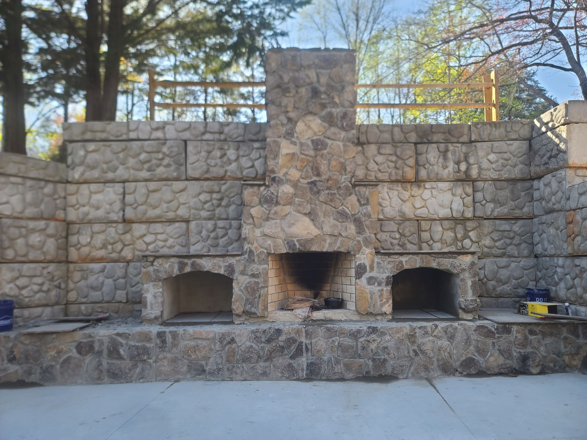 Stone outdoor fireplace with two side ovens, built into a retaining wall.