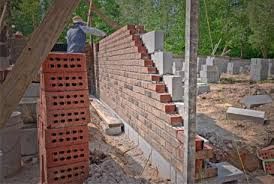 Construction worker laying bricks on a wall, stacks of bricks nearby. Outdoor setting, daytime.