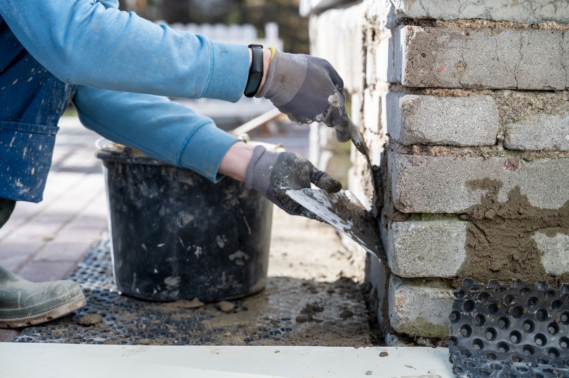 Person wearing work gloves applying mortar to concrete blocks with a trowel.