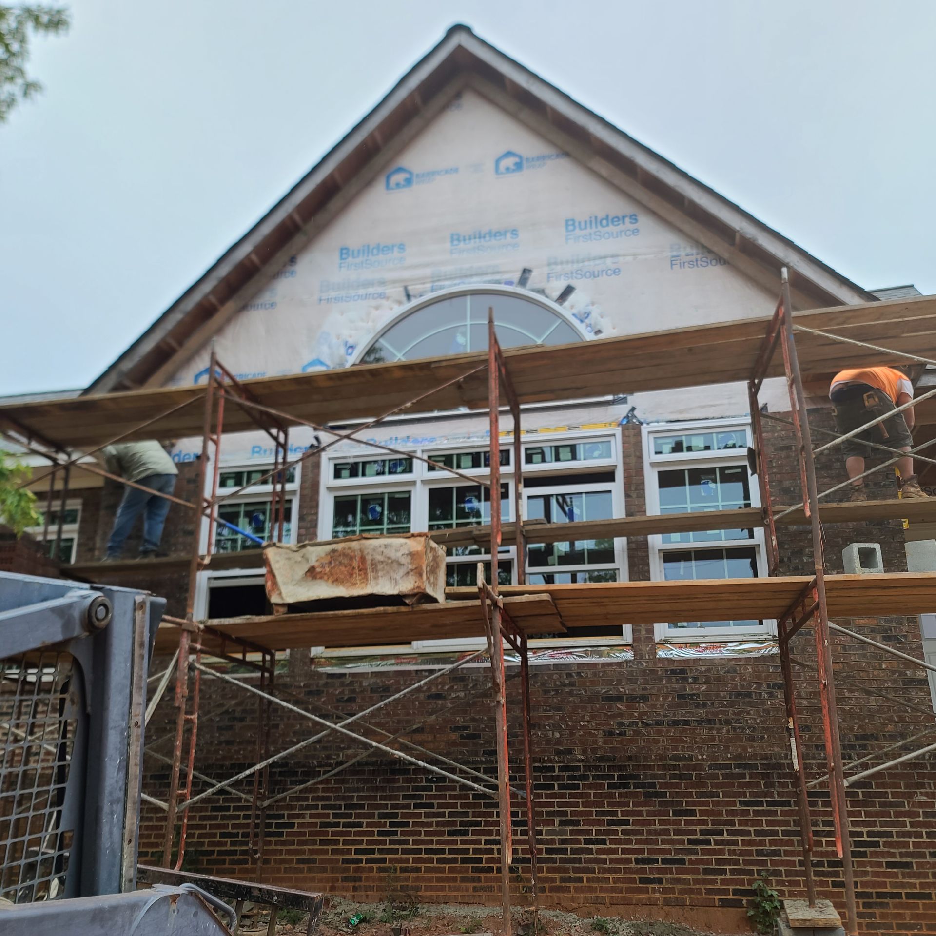 Construction workers on scaffolding renovating a brick building with new windows; cloudy sky.