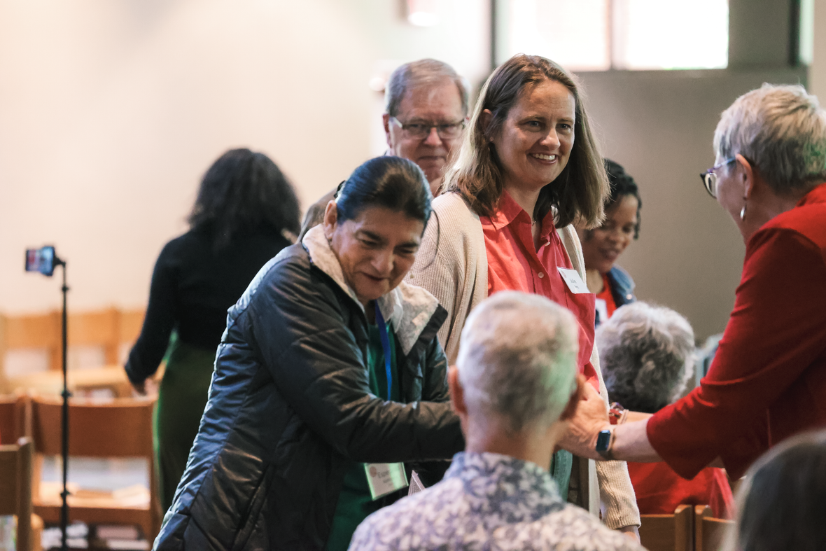 People greeting and shaking hands at an indoor gathering, with smiles and warm conversation