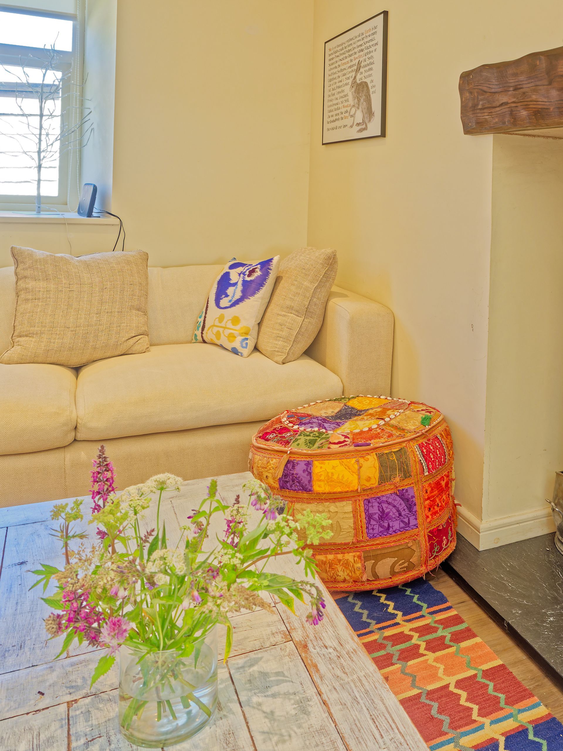 A living room with a couch , ottoman , table and vase of flowers.