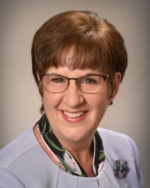 a woman wearing glasses and a purple jacket is smiling for the camera .