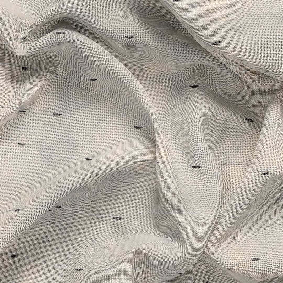A close-up view of light-colored, sheer fabric with a subtle grid pattern and scattered small, dark, horizontal dashes.