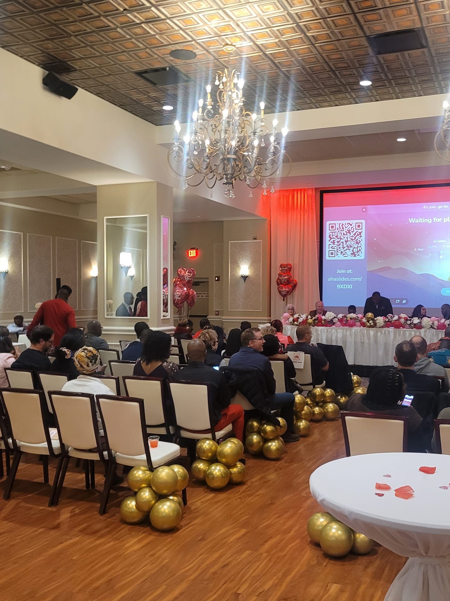 A large room filled with people sitting in chairs and balloons.