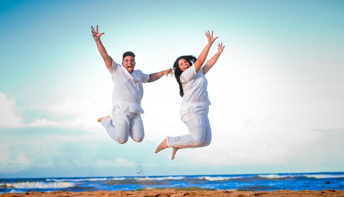 A man and a woman are jumping in the air on the beach.