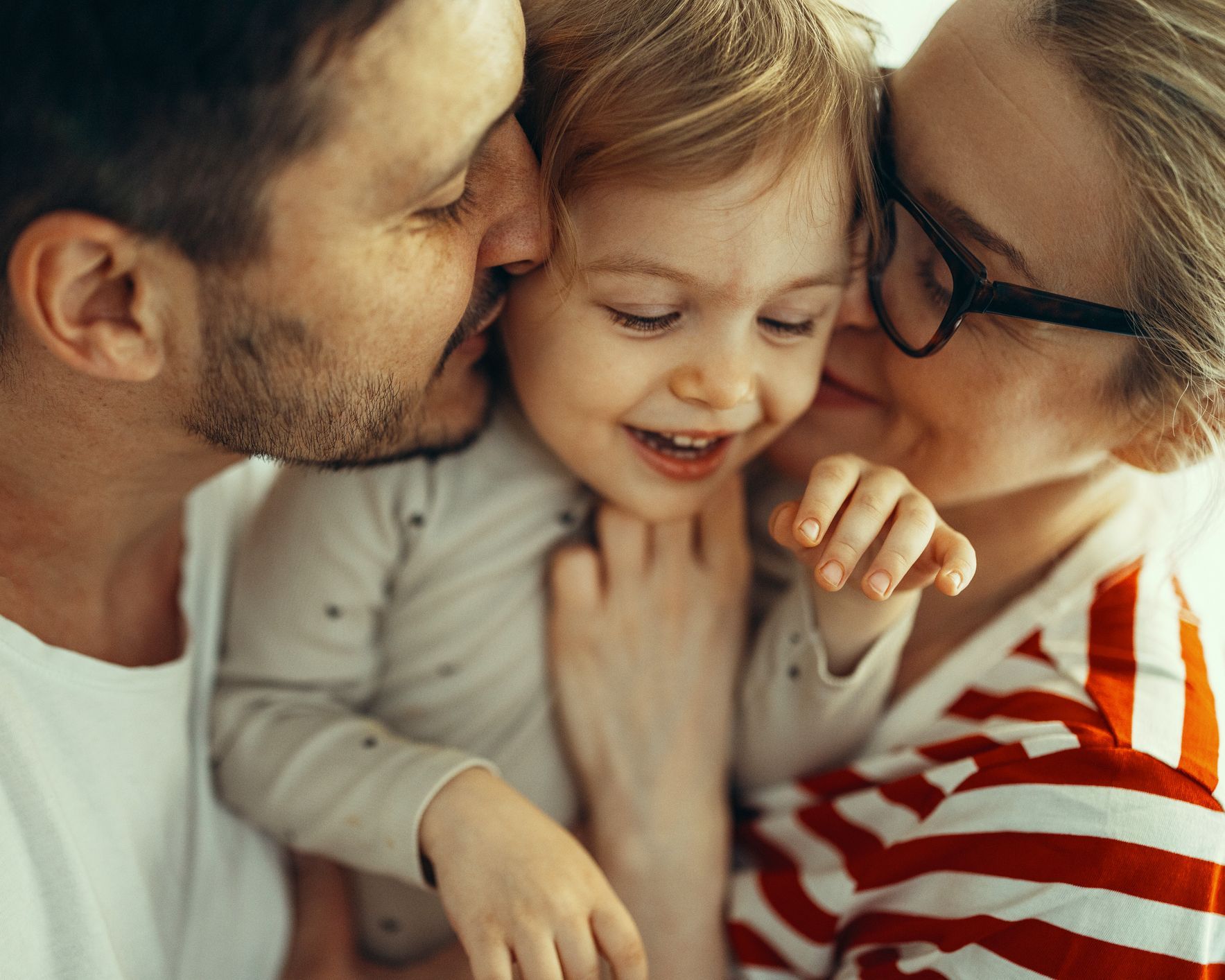 A man and woman lovingly kiss a child.