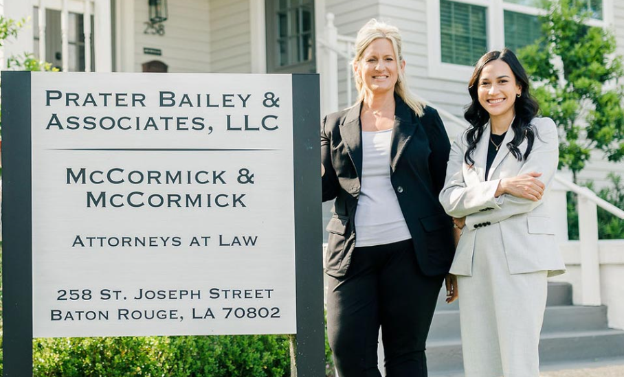 Two women standing in front of a prater bailey & associates llc sign