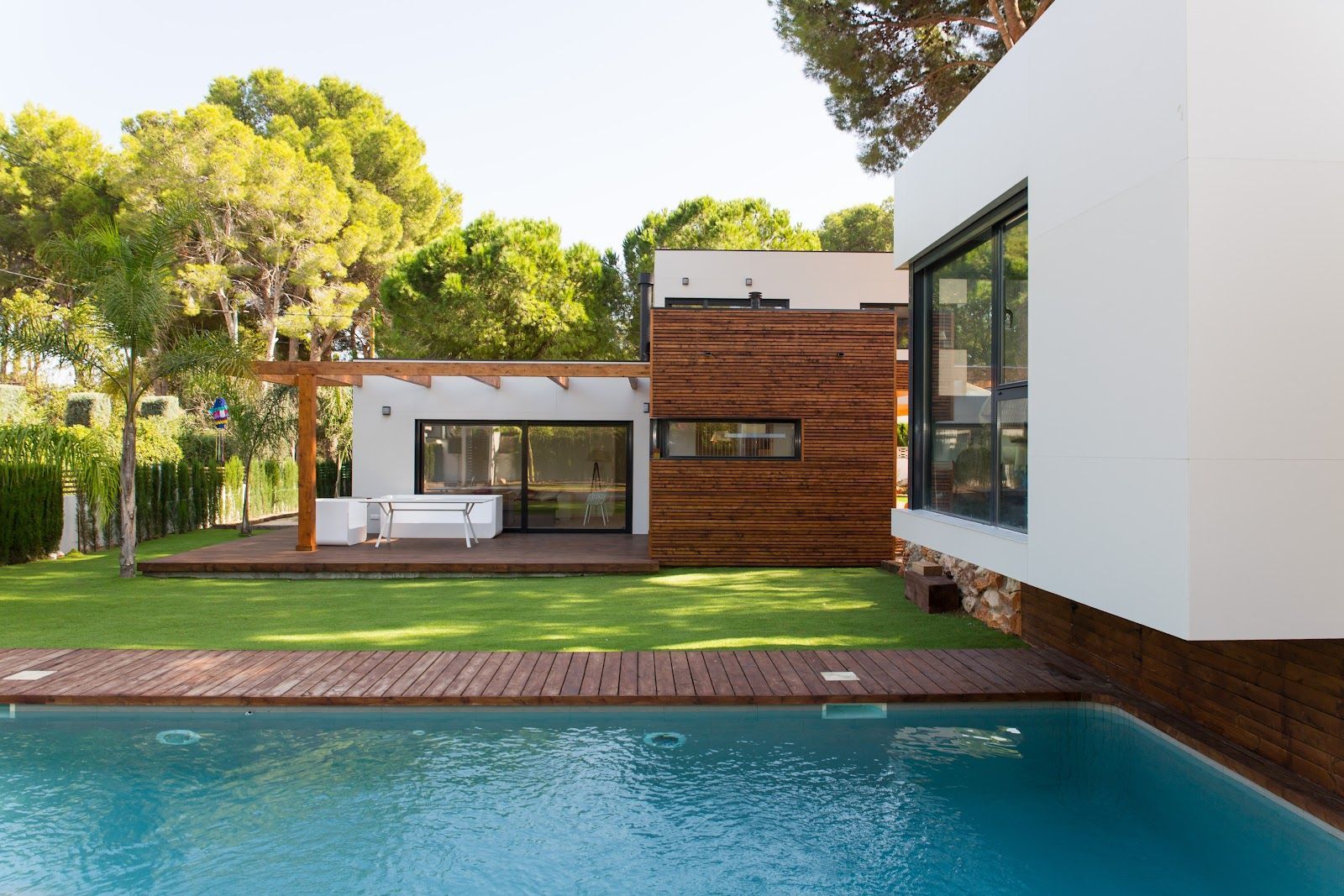 Modern home with pool, lawn, and wooden deck. White and wood exterior with large windows.