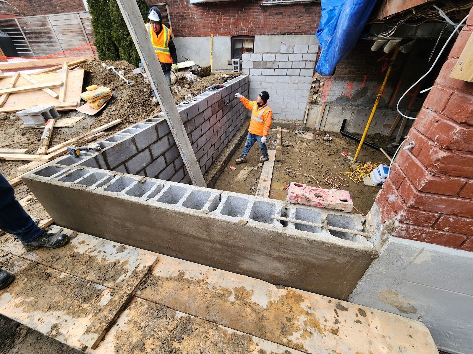 Construction site with workers building a cinder block wall outdoors. One worker is pointing.