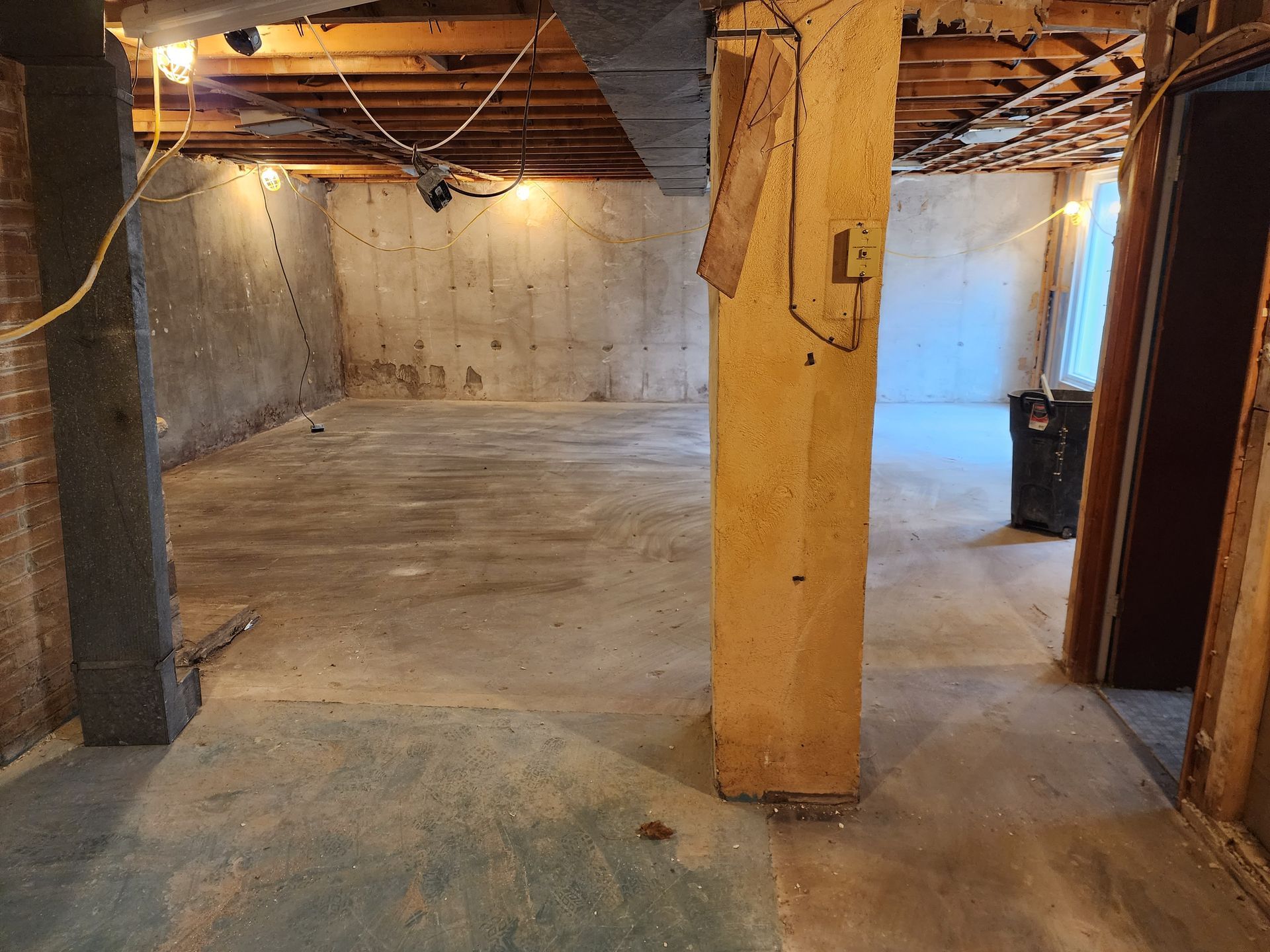 Basement with concrete floor and walls, wooden support beams and columns.