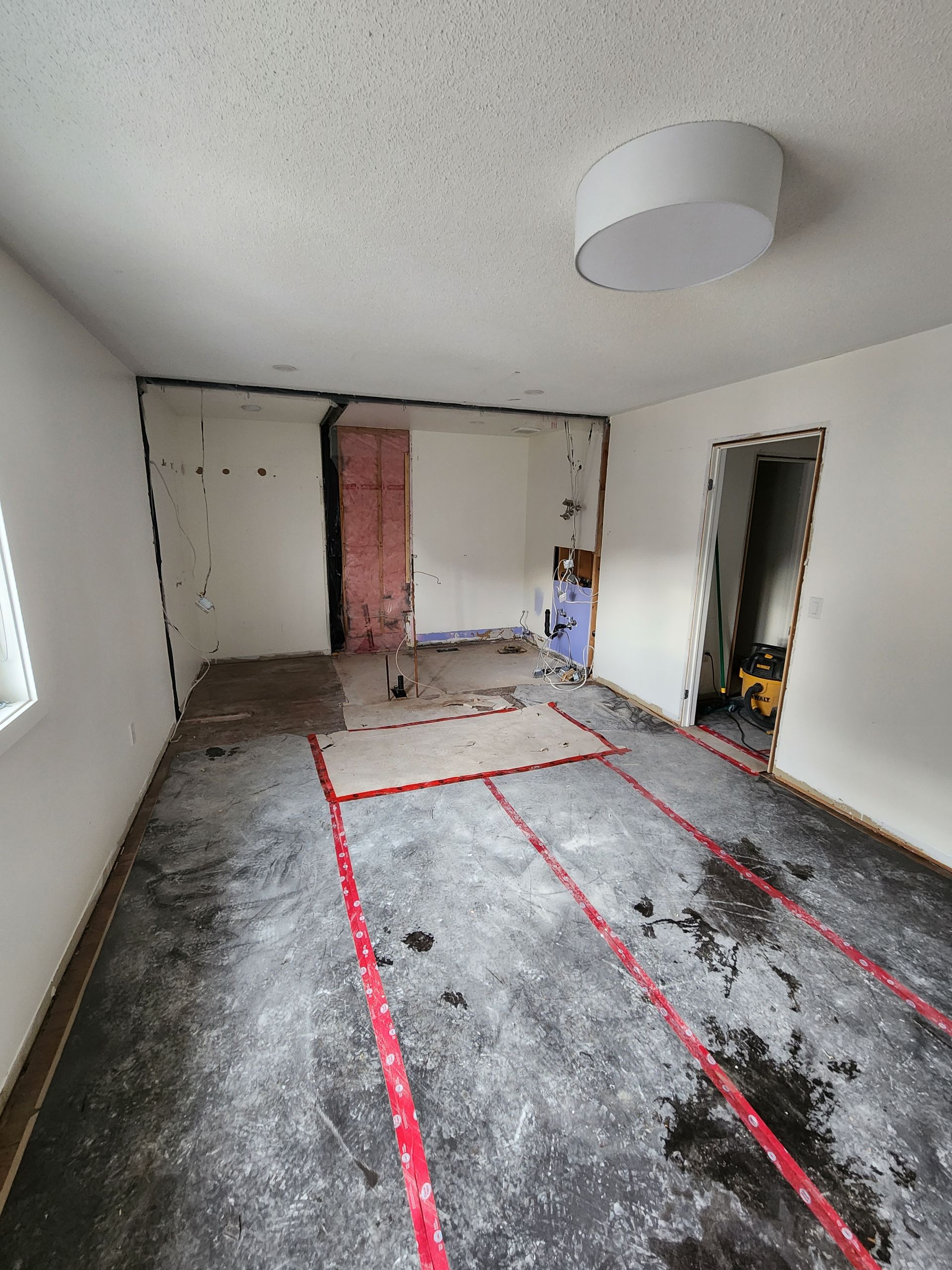 Room undergoing renovation: exposed ceiling beams, damaged flooring, and a chandelier.