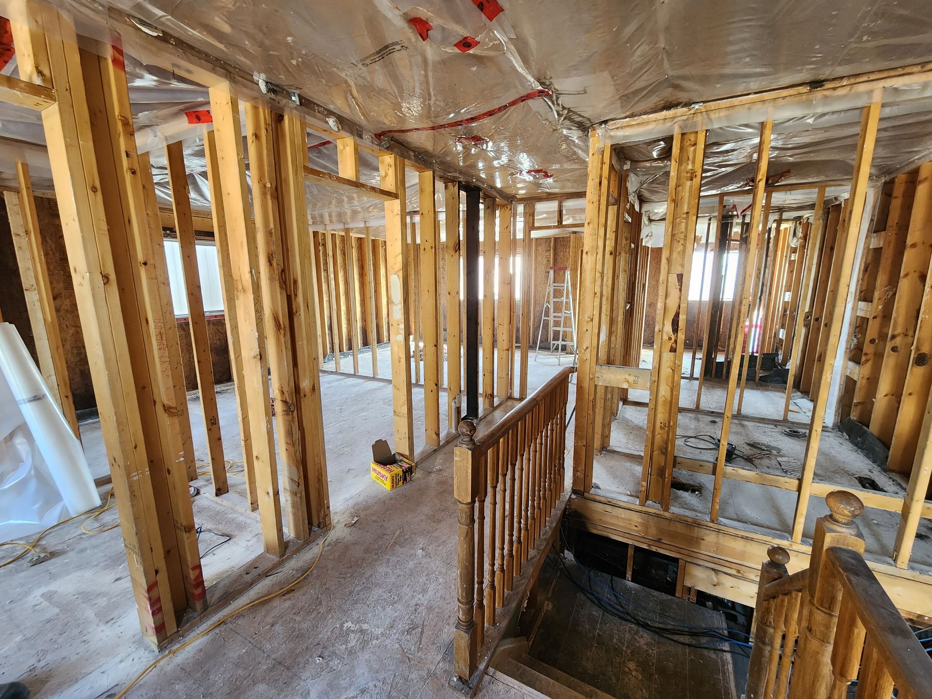 Interior of a building under construction, showing wooden frames and plastic sheeting, with a staircase.