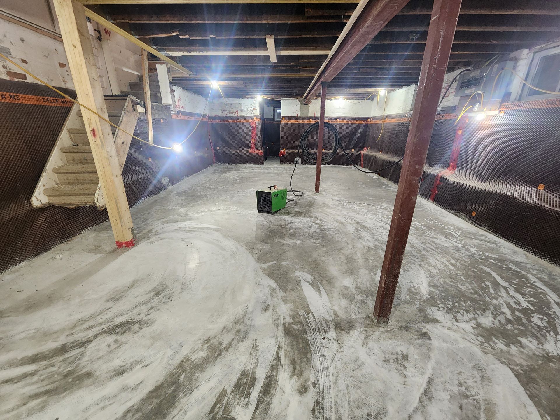 Basement under construction. Concrete floor covered in plastic sheeting. Walls lined with brown insulation.