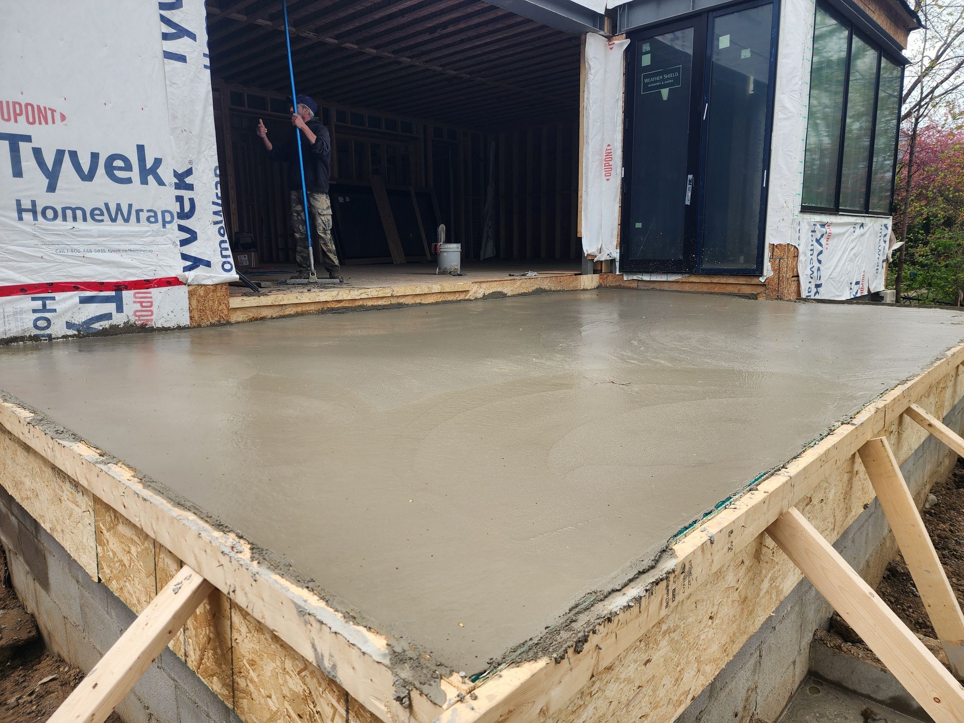 Freshly poured concrete patio with wooden frame, next to a building under construction.