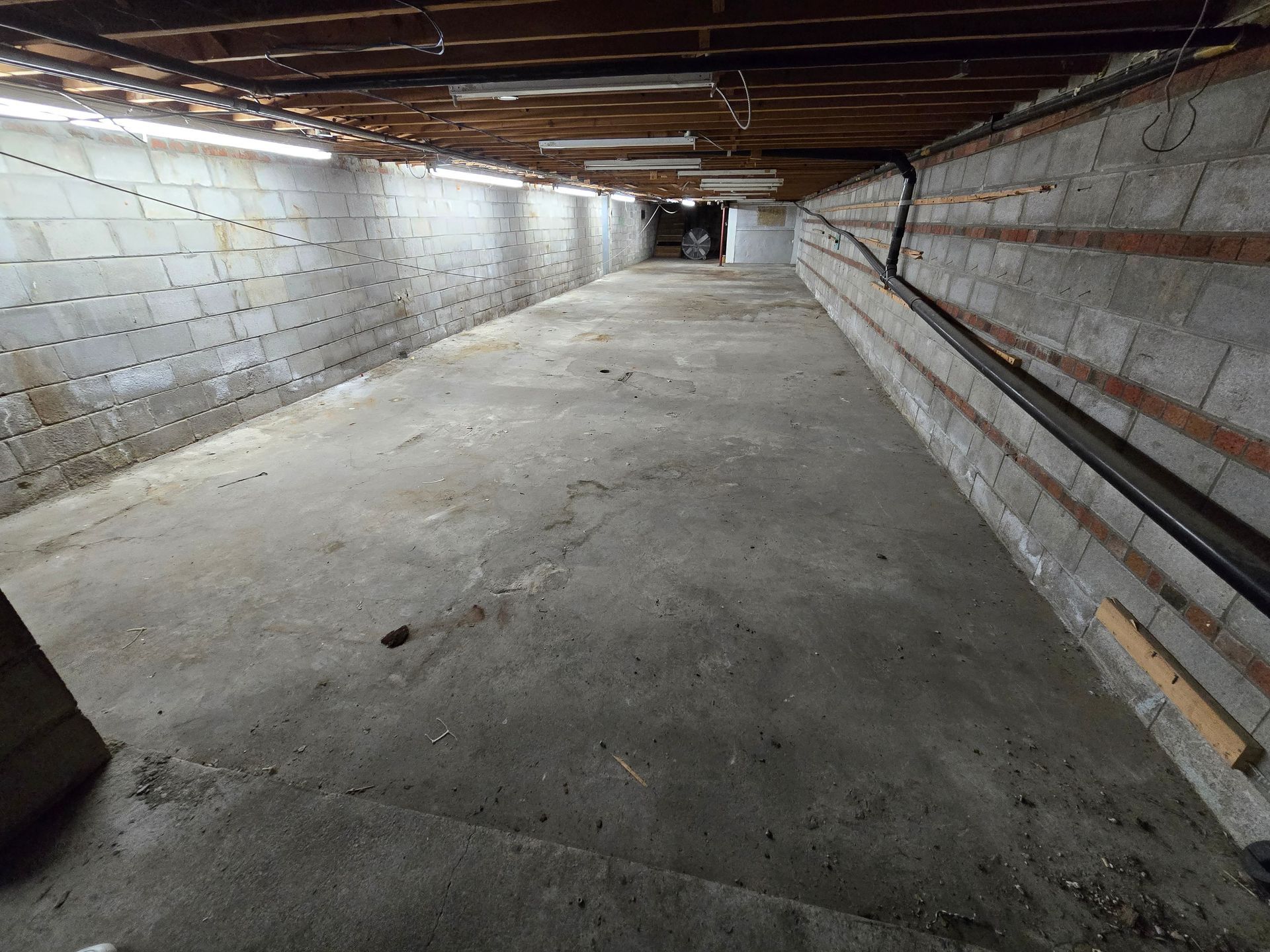 Long, empty, concrete basement. Gray walls and floor. Dim lighting from ceiling fixtures.