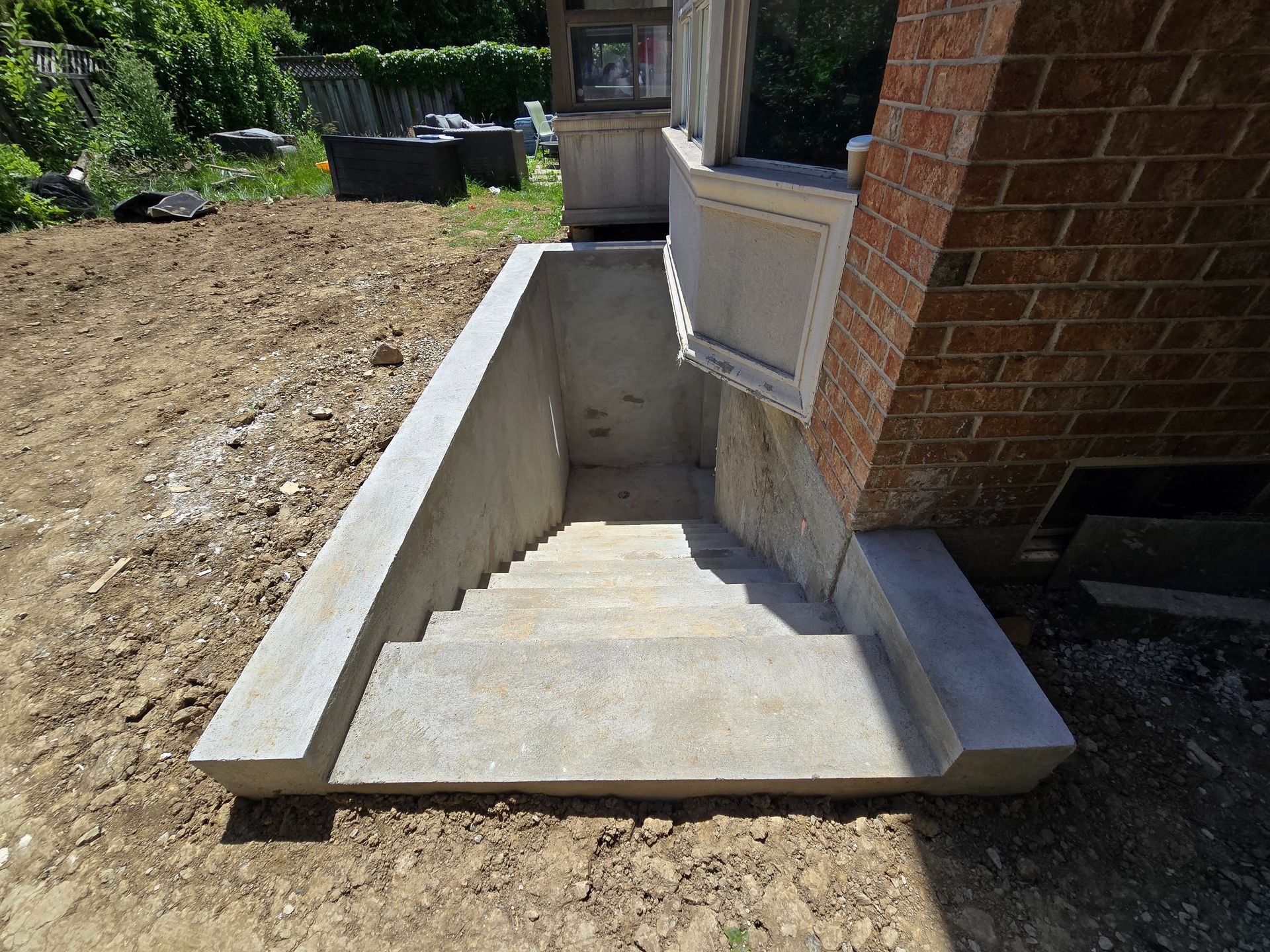 Concrete basement stairs leading down, next to a brick wall.