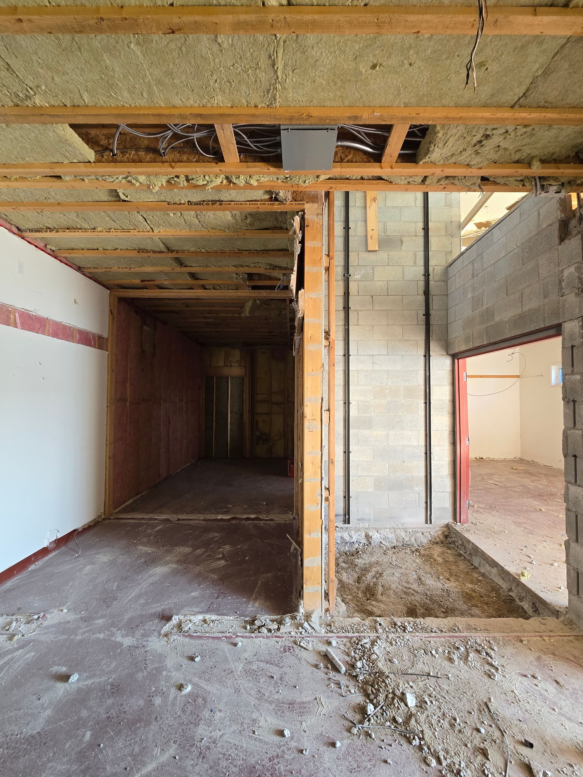 Interior of a building under renovation, showing exposed framing, walls, and debris on the floor.