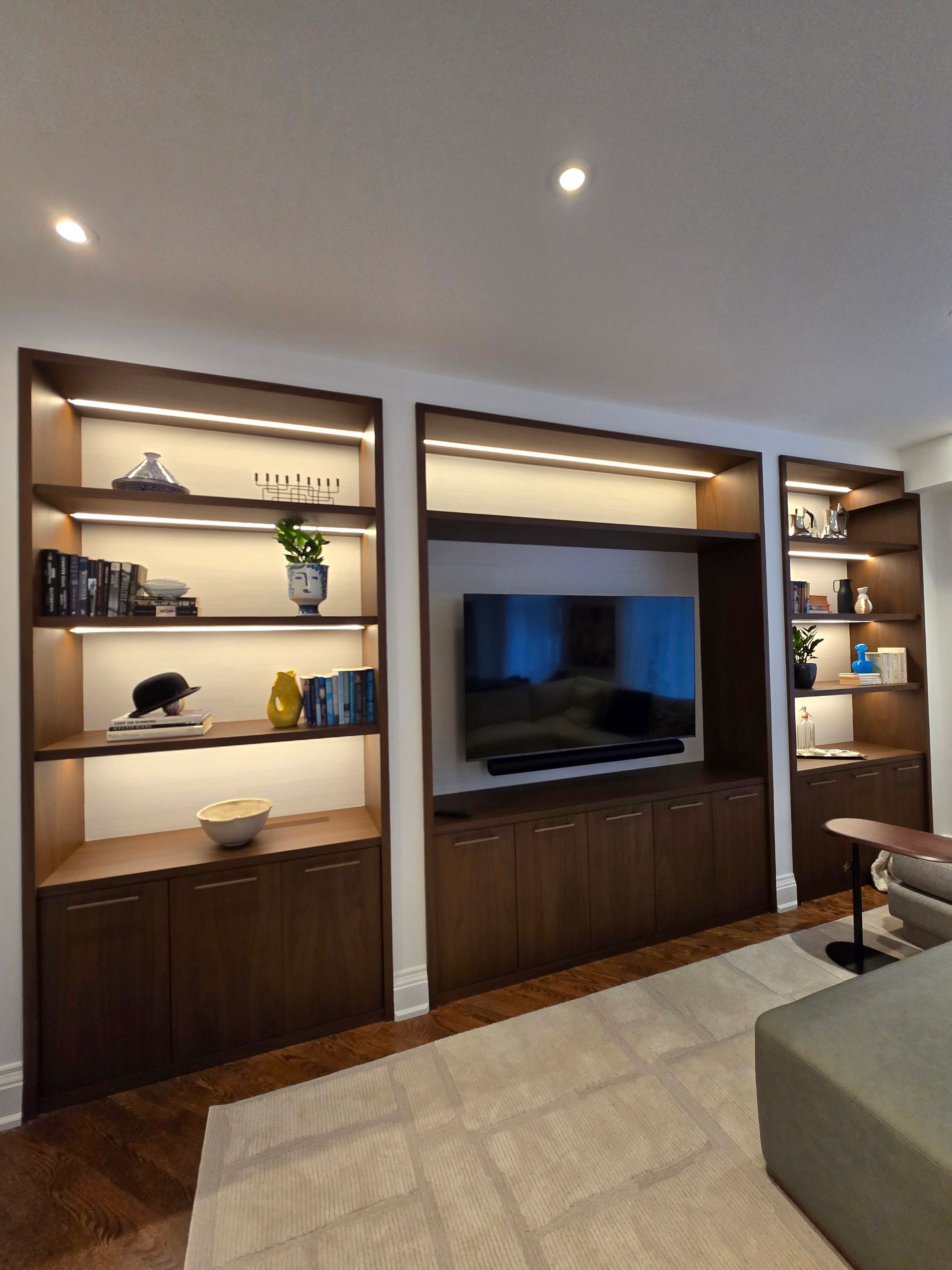 Built-in wooden shelving unit with a TV, recessed lighting, and decorative items.