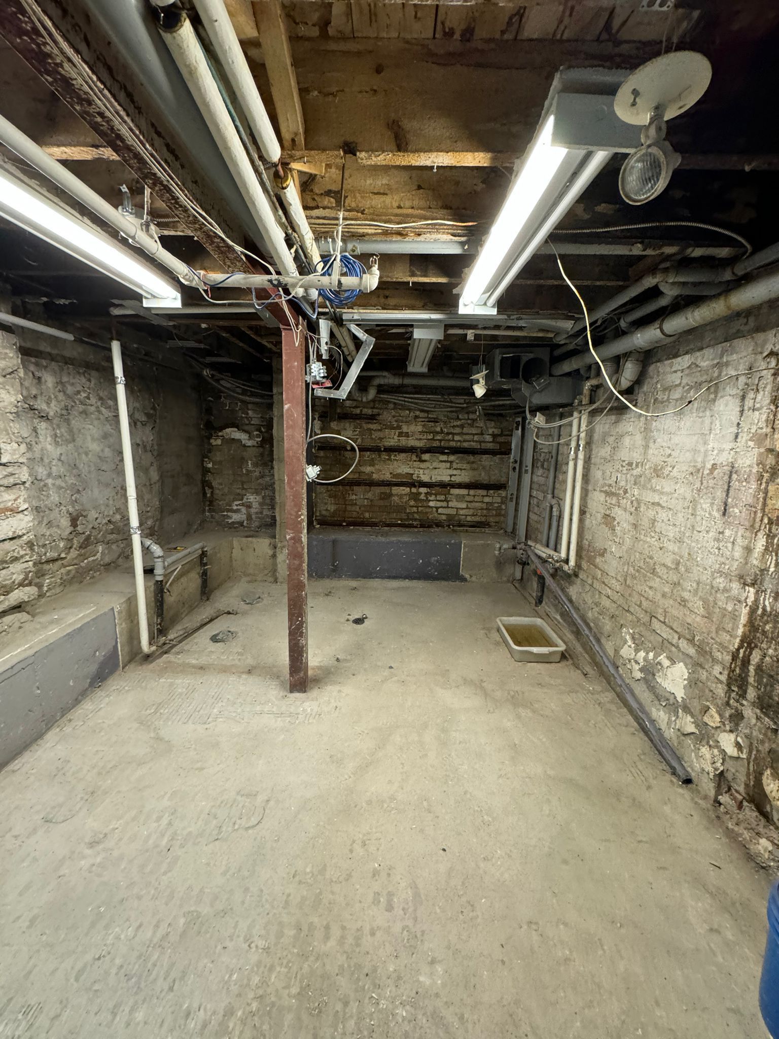 An empty basement with a brick wall and pipes hanging from the ceiling.