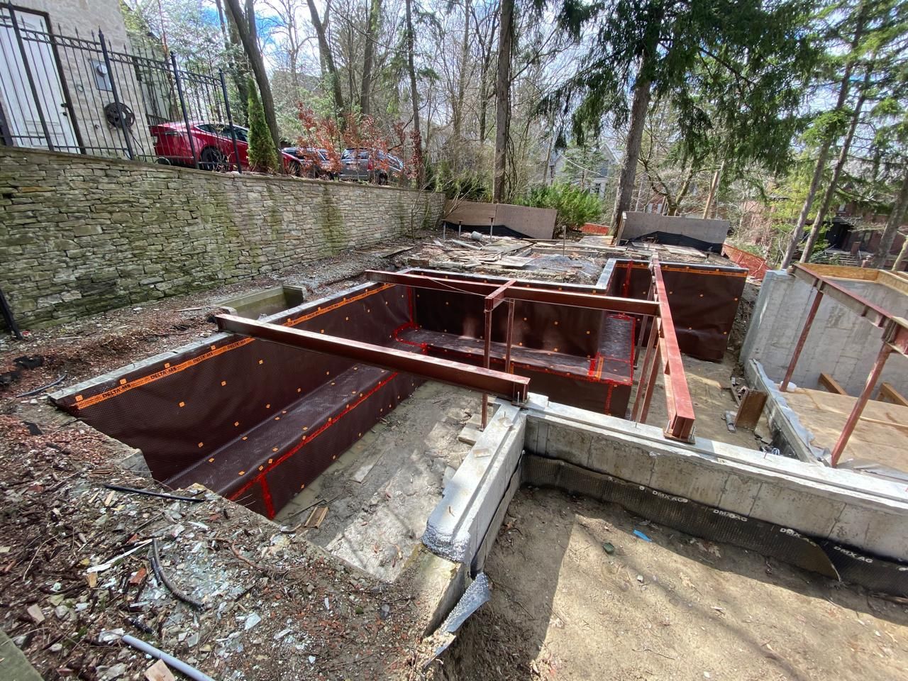 Construction site with wooden forms and concrete foundations, trees in background.