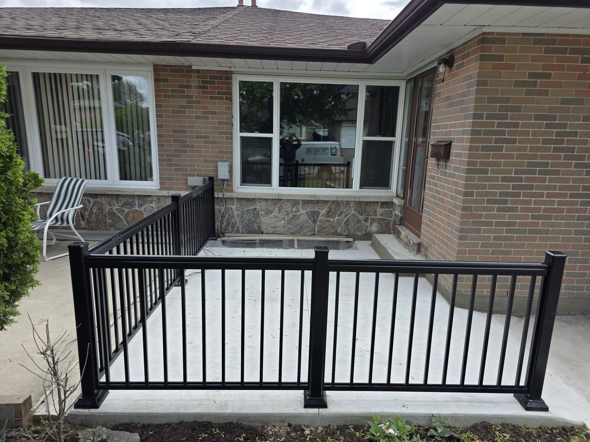 Black railing encloses a concrete patio in front of a brick house with windows.