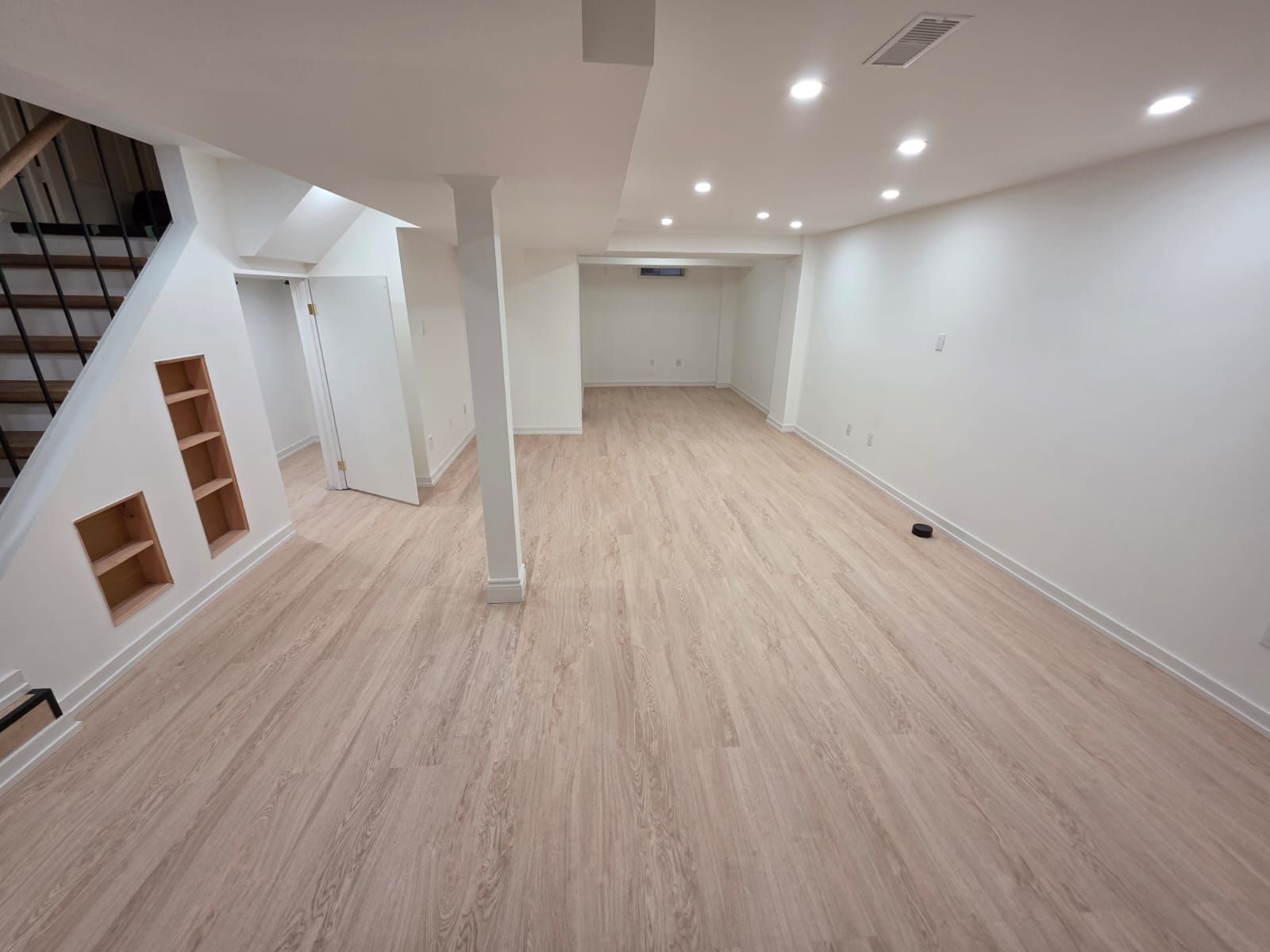 Empty, newly renovated basement with light wood flooring and white walls, recessed lighting.