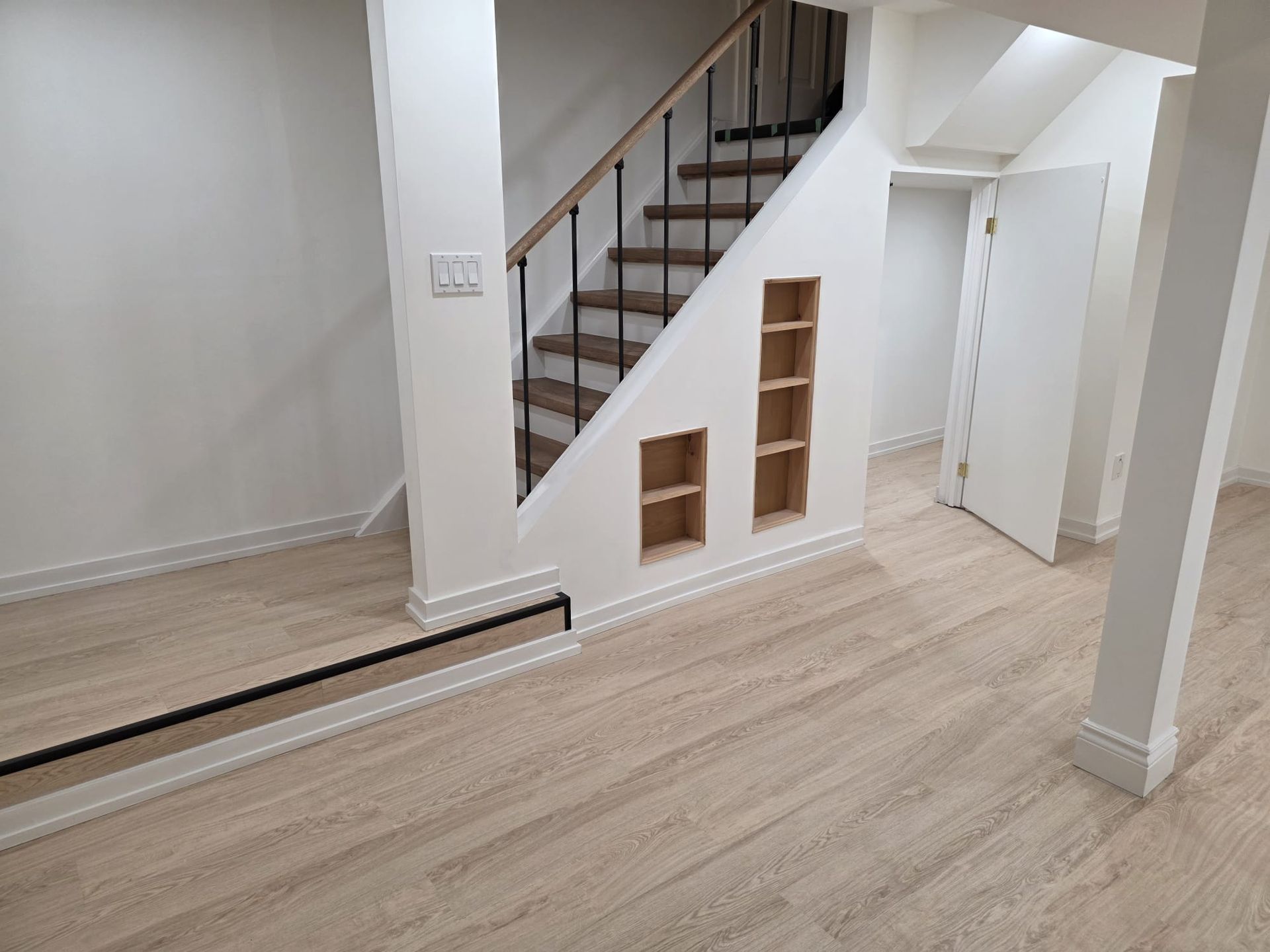 Interior with staircase, built-in shelves, hardwood floors, white walls, and a door.
