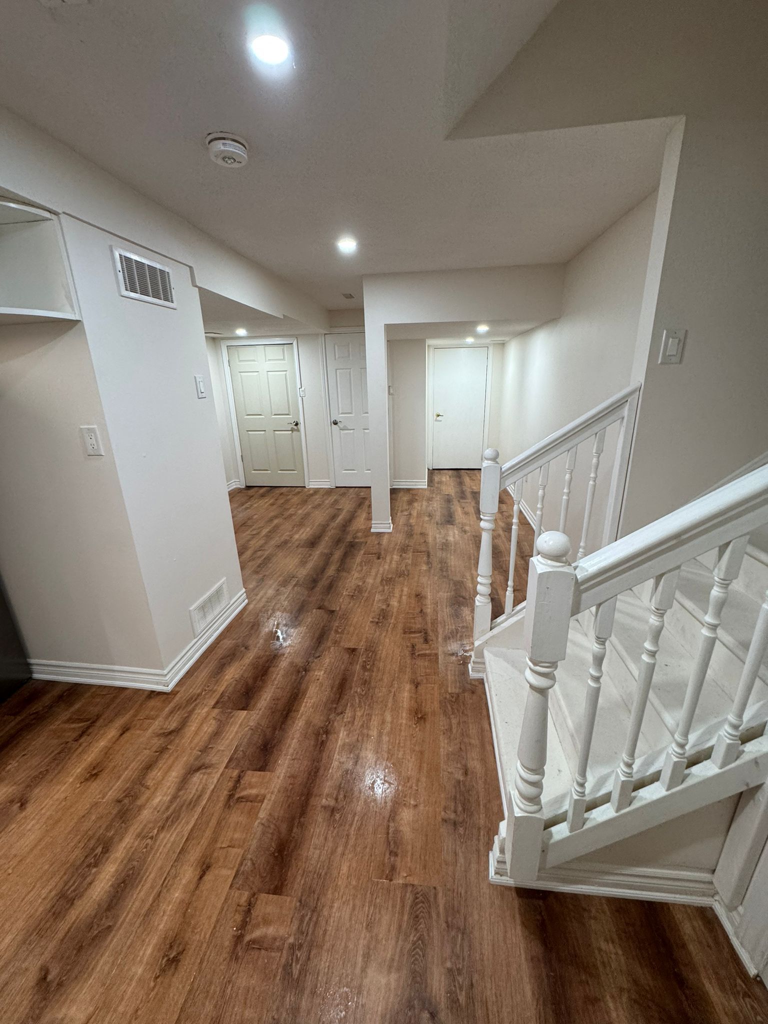 Staircase leading down to a finished basement with wood-look flooring and white walls, doors.